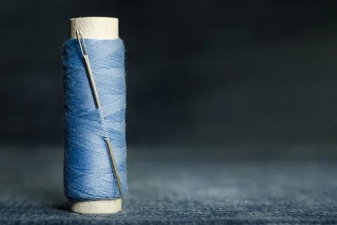 Spool of blue sewing thread with needle on old denim background Stock Photos