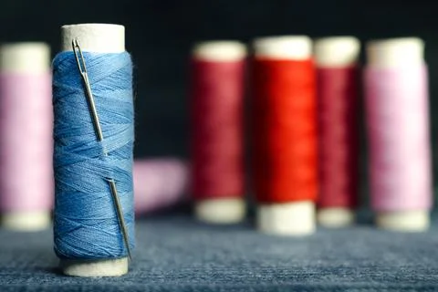 Spool of blue sewing thread with a needle on the background of spools of red Stock Photos