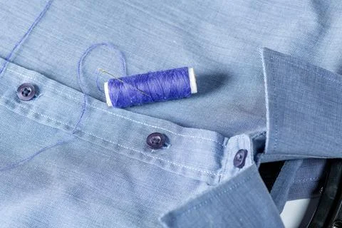 A spool of blue thread and needle on a man's shirt Stock Photos