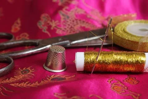 Spool of Gold Thread and Thimble on Vintage Pink Silk Fabric Stock Photos