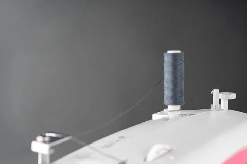 Spool of gray sewing thread stands on top of a white modern sewing machine Stock Photos