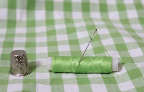 Spool of Green Thread, Thimble and Needle on Green Checkered Fabric Stock Photos