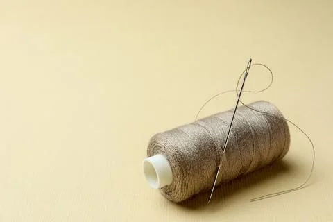Spool of grey sewing thread with needle and thimble on beige background. Sp.. Stock Photos