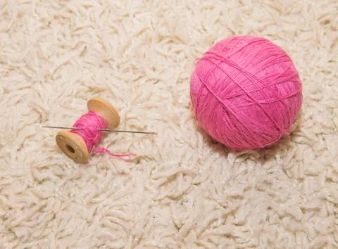 A spool of pink thread with a needle and a ball of wool lies on a white backg Stock Photos