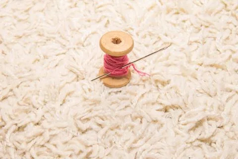 A spool of pink thread with a needle lies on a white background Stock Photos