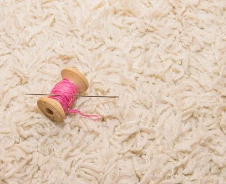 A spool of pink thread with a needle lies on a white background Stock Photos