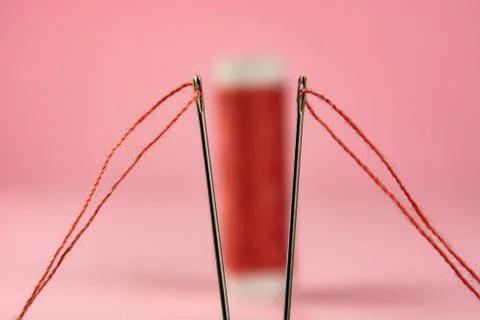 Spool with red thread and needle on pink background Stock-Fotos