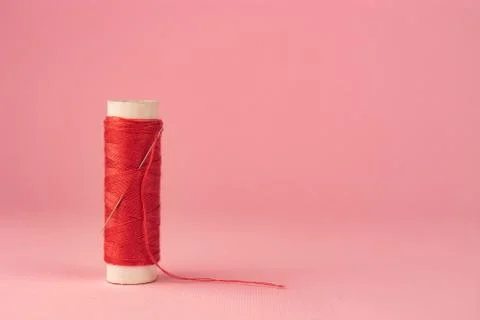 Spool with red thread and needle on pink background Foto stock