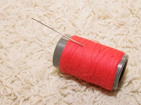 A spool of red thread with a needle lies on a white background Stock Photos