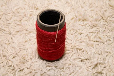 A spool of red thread with a needle lies on a white background Stock Photos
