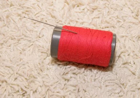A spool of red thread with a needle lies on a white background Stock Photos
