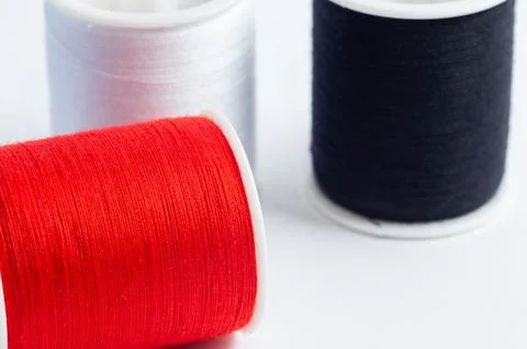 A spool of red thread with a needle, set against a background of spools of .. Foto stock