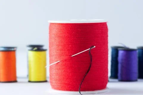 A spool of red thread with a needle, set against a background of spools of .. Foto stock