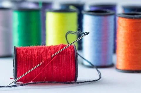 A spool of red thread with a needle, set against a background of spools of .. Foto stock