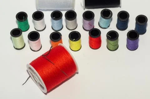 A spool of red thread with a needle, set against a background of spools of .. Foto stock