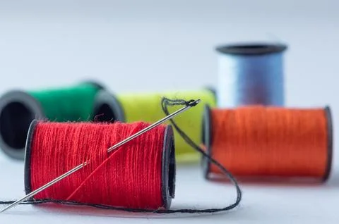 A spool of red thread with a needle, set against a background of spools of .. Foto stock
