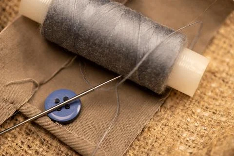 A spool of sewing thread and a sewing needle on a fabric background. Close-up Stock Photos