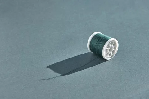 A spool of sewing thread in rich emerald color lies with unwound thread on a  Fotos Stock