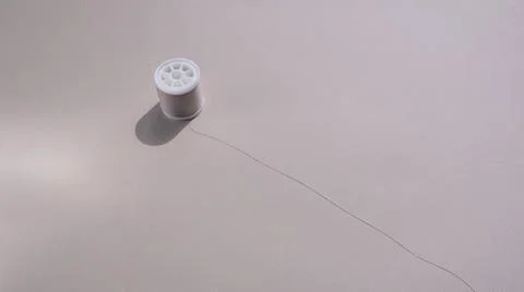 A spool of sewing thread in a soft beige color on a harmonious sandy backgrou 스톡 사진