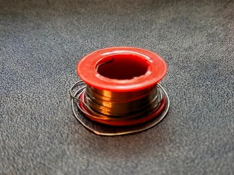 A spool of shiny, copper-colored wire resting on a textured dark surface, w.. Stock Photos