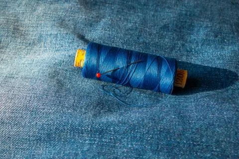 Spool of thread on a blue jeans with a round head pin put in the spool Foto stock