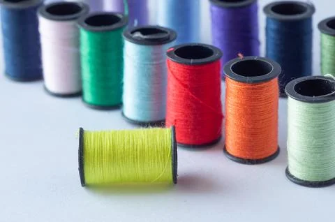 A spool of thread with a needle, set against a background of spools of colo.. Foto stock