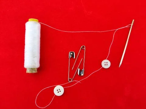 Spool of white thread, white buttons,needle and safety pins on red background Stock Photos