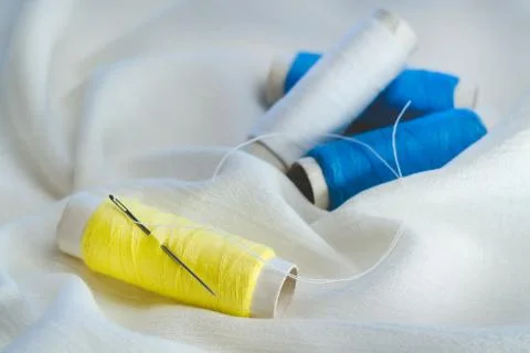 A spool of yellow threads with a sewing needle on white cotton cloth Stock Photos