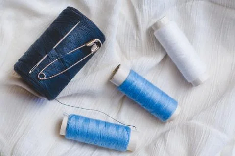 Spools of blue and white thread with sewing needle and pin on white cotton Stock Photos