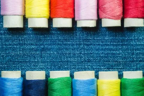Spools of colored sewing thread arranged in two rows on denim with copy space Foto stock