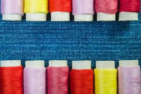Spools of colored sewing thread arranged in two rows on blue denim Stock Photos