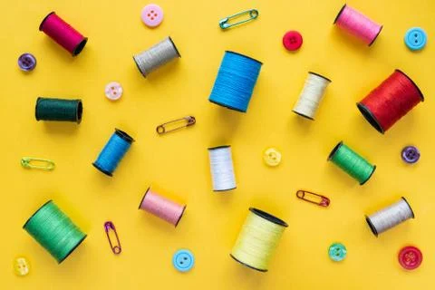 Spools of colored thread, buttons and safety pins on yellow background Stock Photos