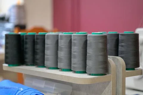 Spools of gray thread sit on a wooden rack Stock Photos