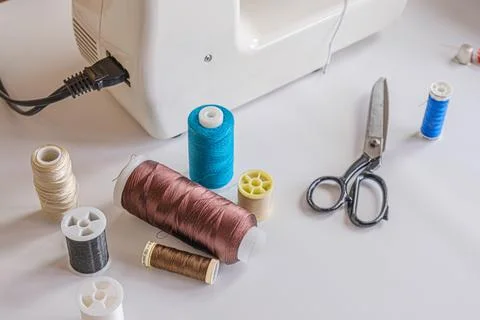 Spools of multi-colored thread and scissors on the table next to the electric Stockfoto's
