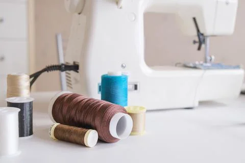 Spools of multi-colored thread on the table next to the electric sewing machi Stock Photos
