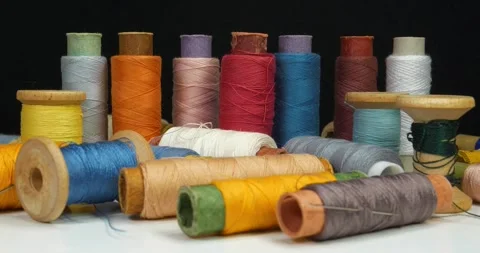 Spools of multi-colored threads lies on table and rotates on black background Video stock 309103571