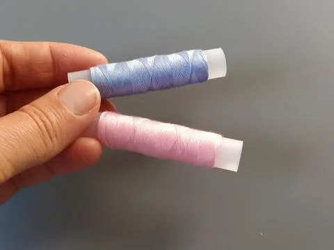 Spools of pink and blue thread on a woman's hand. Textile industry. Gray back Stock Photos