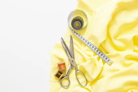 Spools of thread, measuring tape, sewing scissors and yellow fabric on a whit Stock Photos