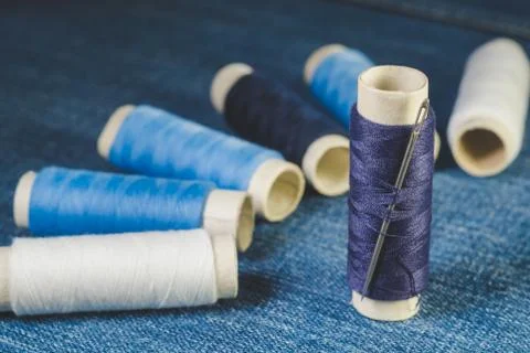 Spools of white and blue threads and sewing needle on denim Stock Photos