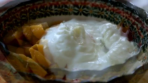 Spoon adding yogurt to a bowl of cut peach pieces and stirring them together. Stock Footage 338258208