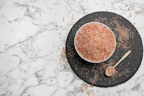 Spoon and bowl with pink himalayan salt on white marble table, flat lay. Spac Stock Photos