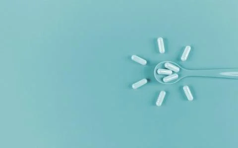 Spoon and capsules on blue backdrop with copy space. Monochrome flat lay. Stock Photos