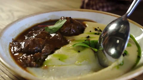 With a spoon, beautifully peels off a layer of potatoes with green butter, beef Stock Footage 140986734