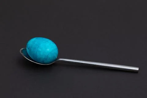 Spoon with an blue easter egg lies on a dark base Stock Photos