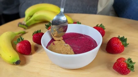 Spoon Dropping Peanut Butter into Acai Smoothie Bowl with Strawberries and Stock Footage 320466473