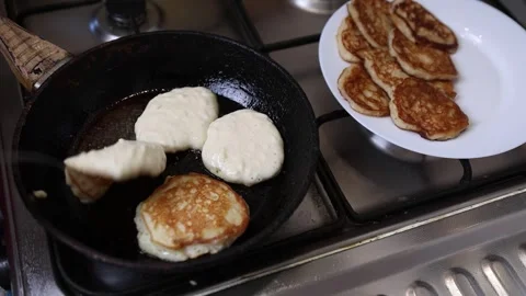 A spoon drops batter onto a hot frying pan with golden pancakes, while a plat Vídeos de archivo 316809506
