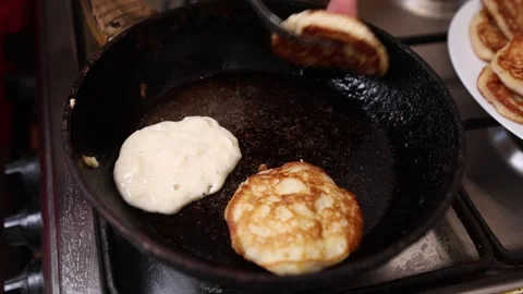 A spoon drops batter onto a hot frying pan with golden pancakes, while a plat Vídeos de archivo 316809517