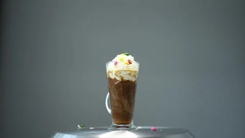 A spoon elegantly hovers over a glass mug filled with rich coffee, topped with w Stock Footage 300021779