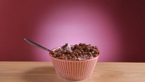 Spoon falls into a deep bowl filled with chocolate corn balls and milk. Flakes Video stock 149133762