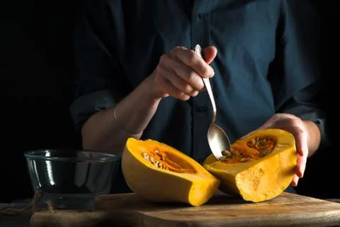 Spoon in hand, pumpkin halves on a table on a blue background Stock Photos
